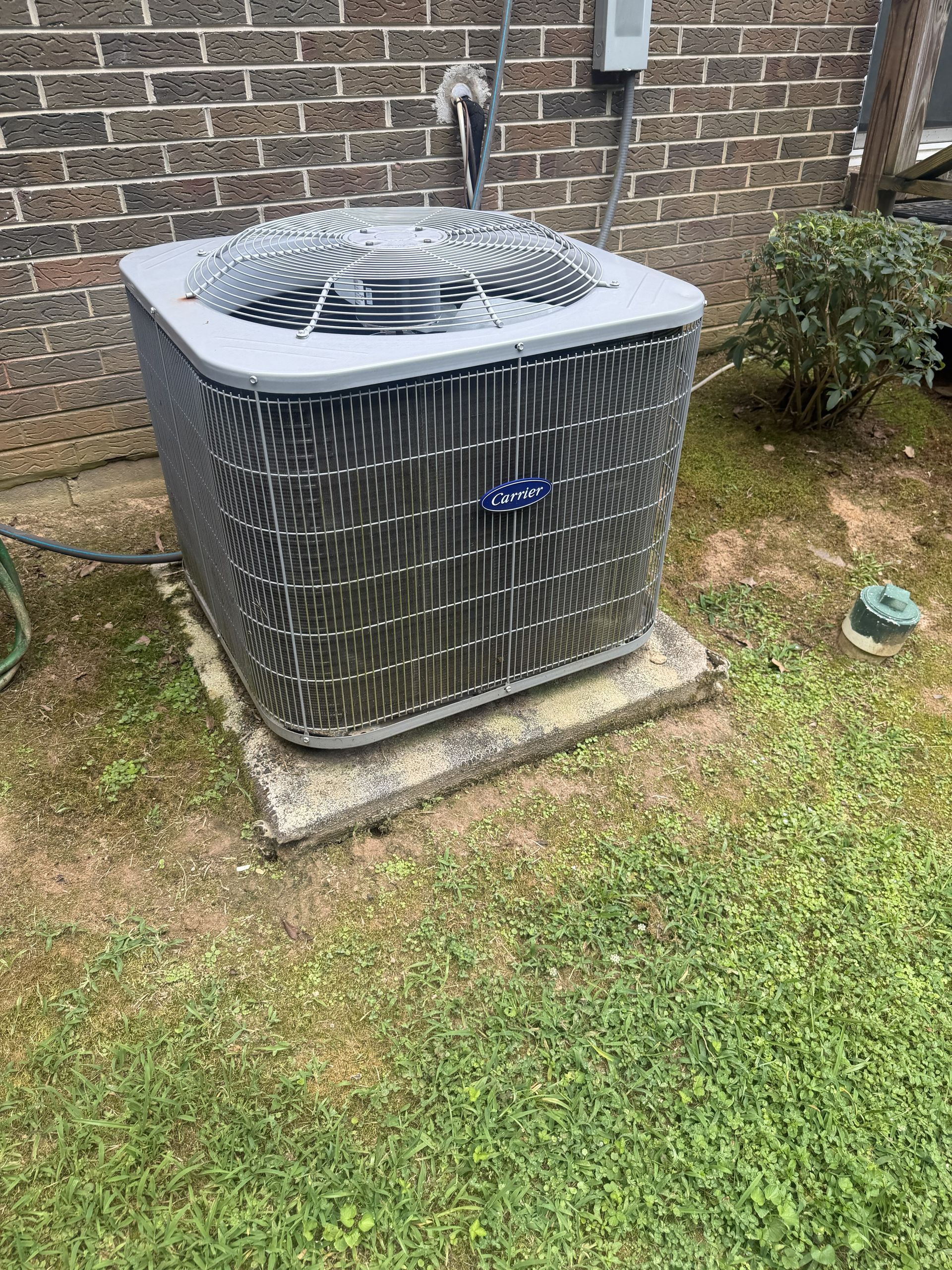 Outdoor air conditioner unit beside a brick wall on a grassy lawn