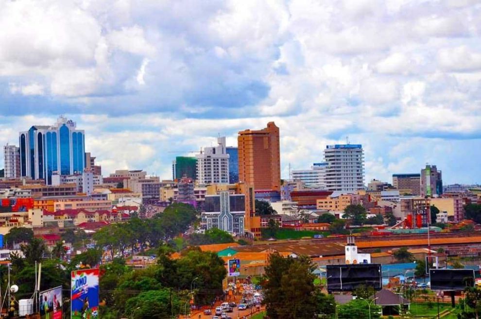 City skyline with colorful high-rise buildings under a cloudy sky, seen above a dense urban neighborhood
