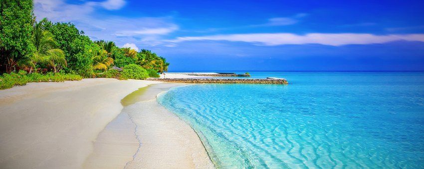 Tropical beach with turquoise water, white sand, and lush green vegetation under a bright blue sky.