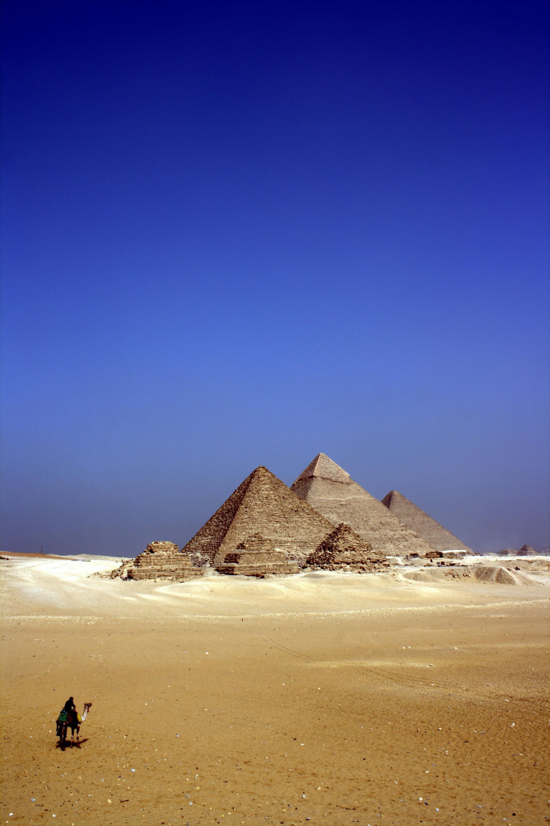 Pyramids of Giza under a clear blue sky, with a person riding a camel in the foreground.