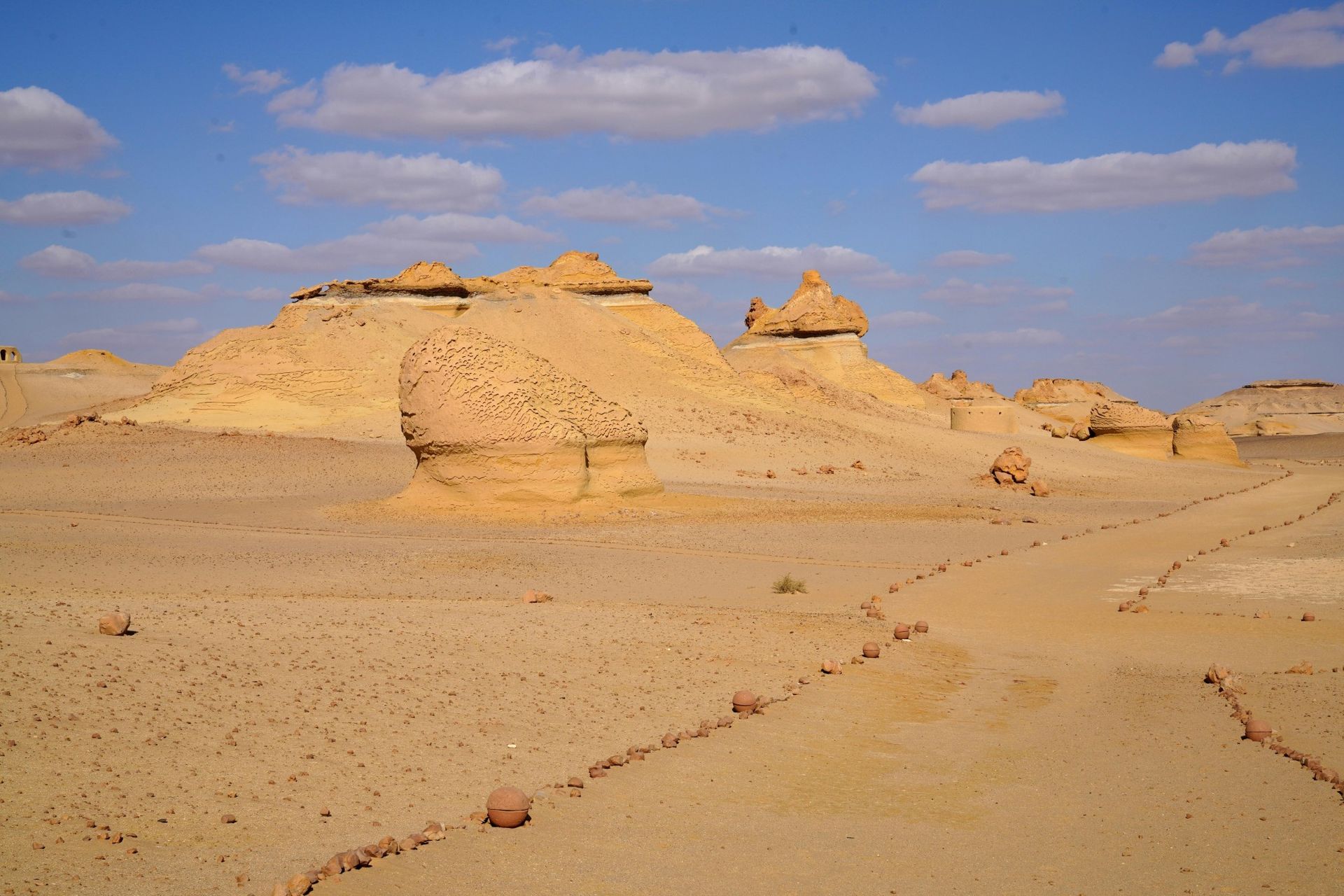 Desert landscape with rock formations under a blue sky dotted with clouds.