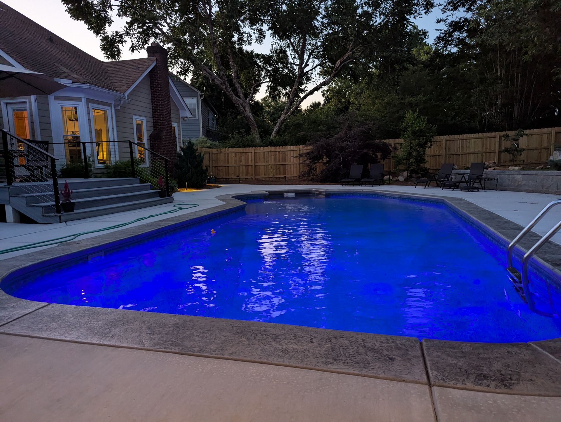 Backyard swimming pool glowing blue at dusk beside a patio and house