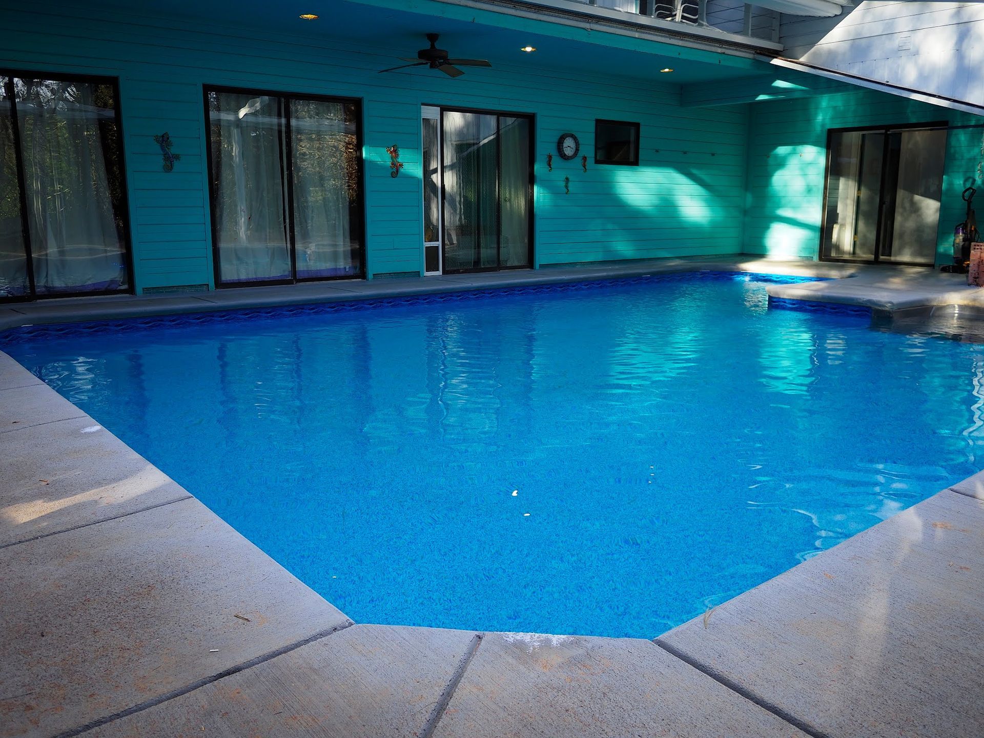 Empty blue swimming pool beside a building with sliding glass doors and windows