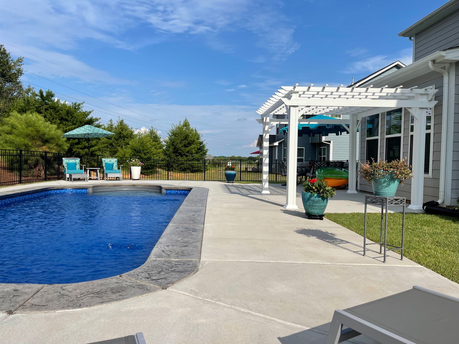 Backyard pool with blue water, patio chairs, and a white pergola beside a modern house