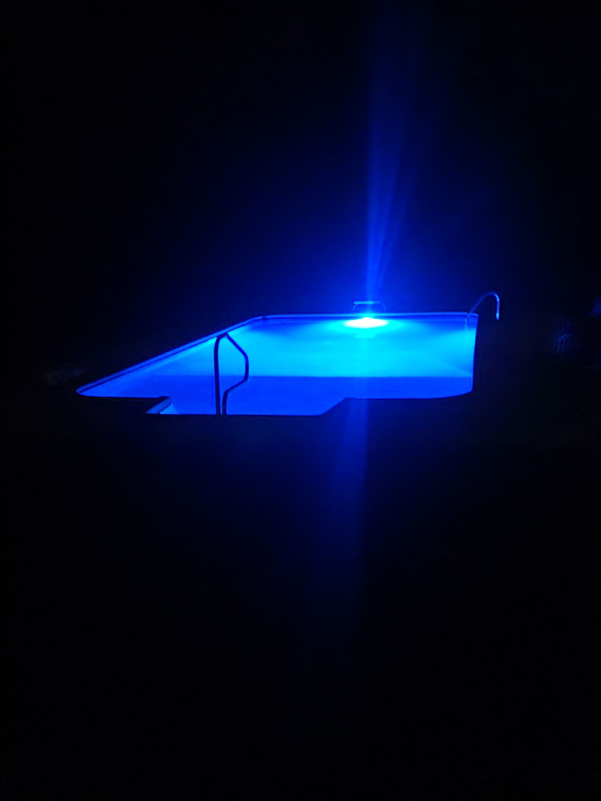 Blue-lit stage or pool at night with a bright spotlight and dark surroundings