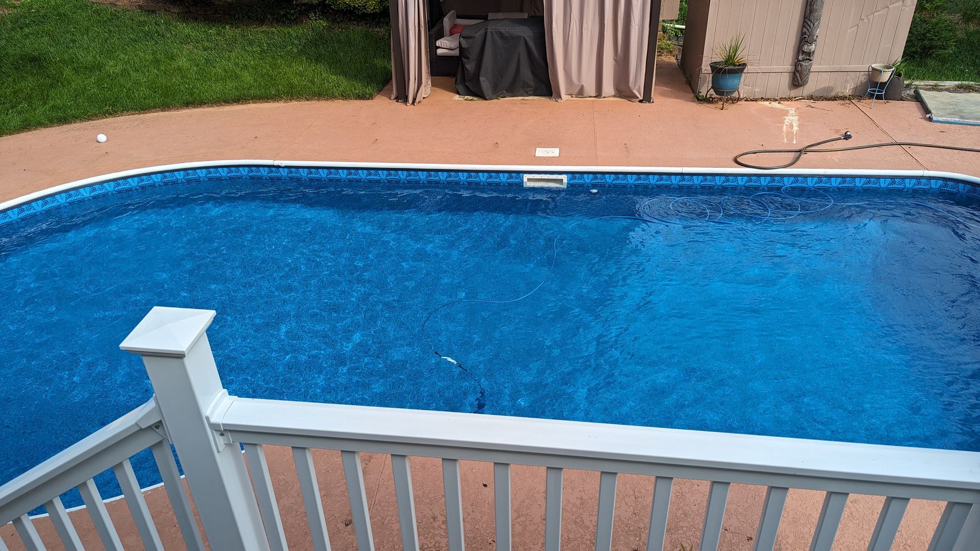 Backyard swimming pool with clear blue water, viewed over a white railing from a patio.