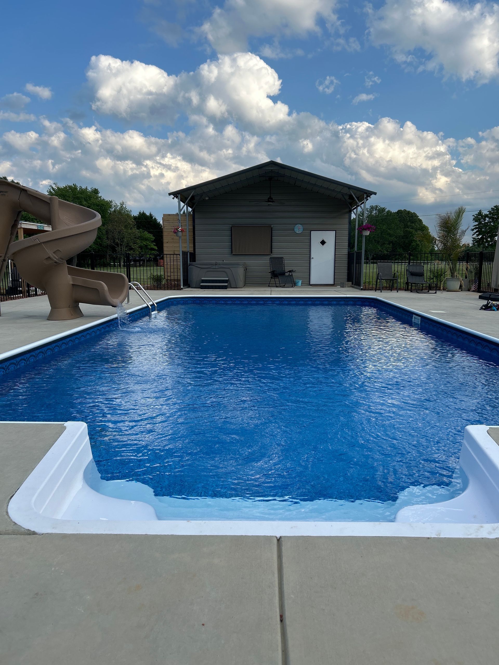 Backyard swimming pool with a slide, pool house, and cloudy sky