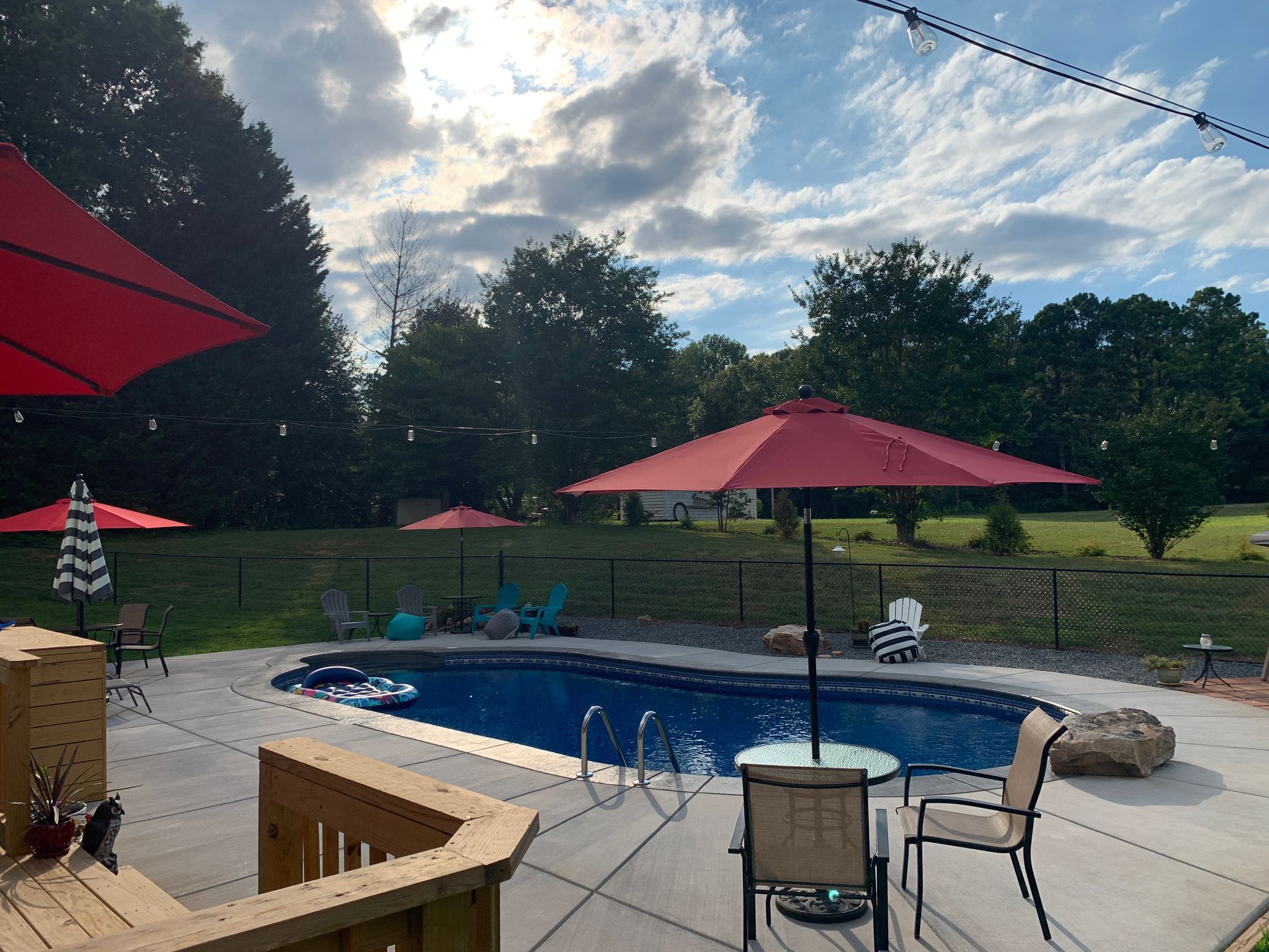 Backyard pool with red umbrellas, chairs, and a cloudy sky at dusk