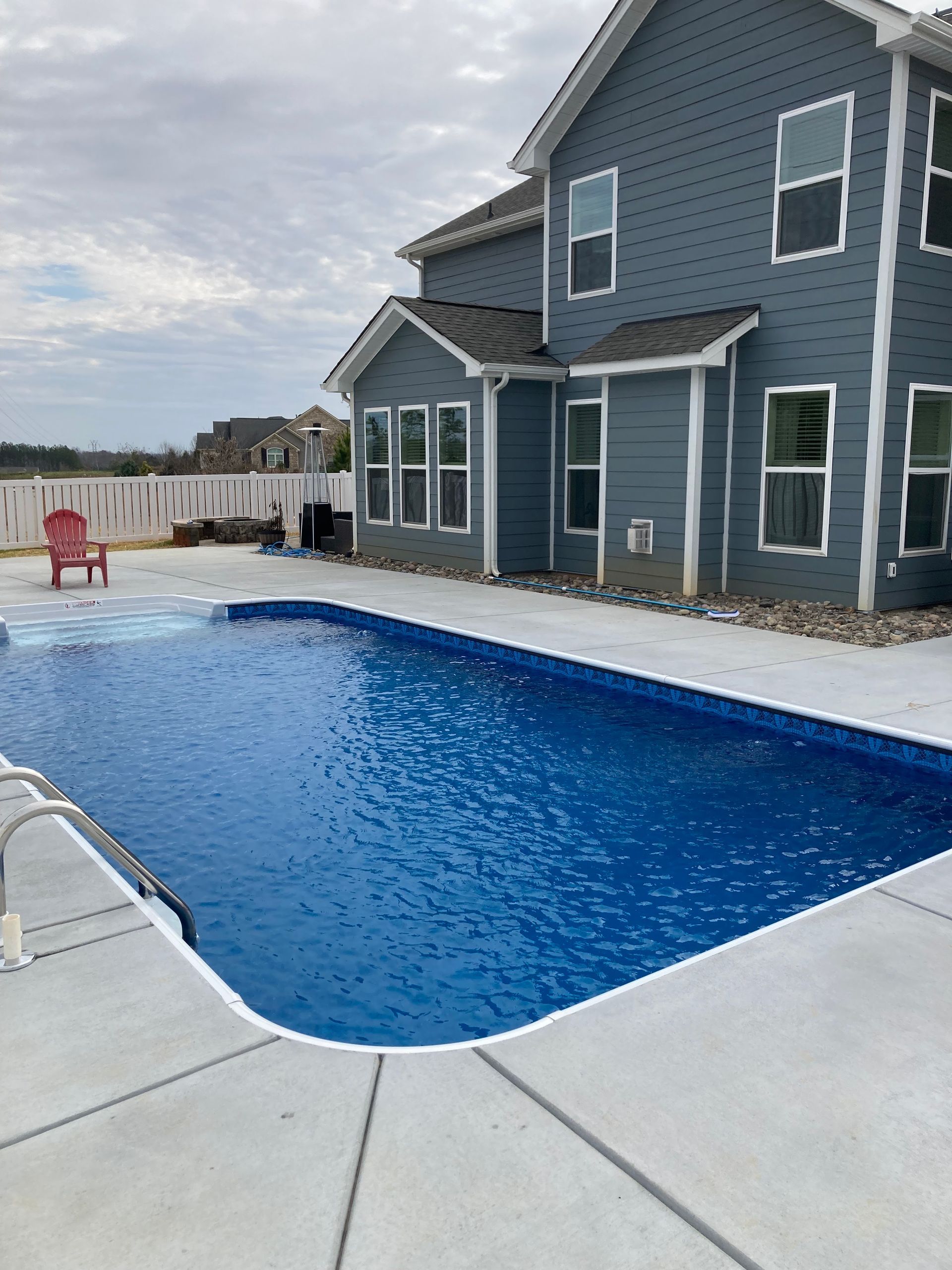 Backyard pool beside a blue two-story house under cloudy skies