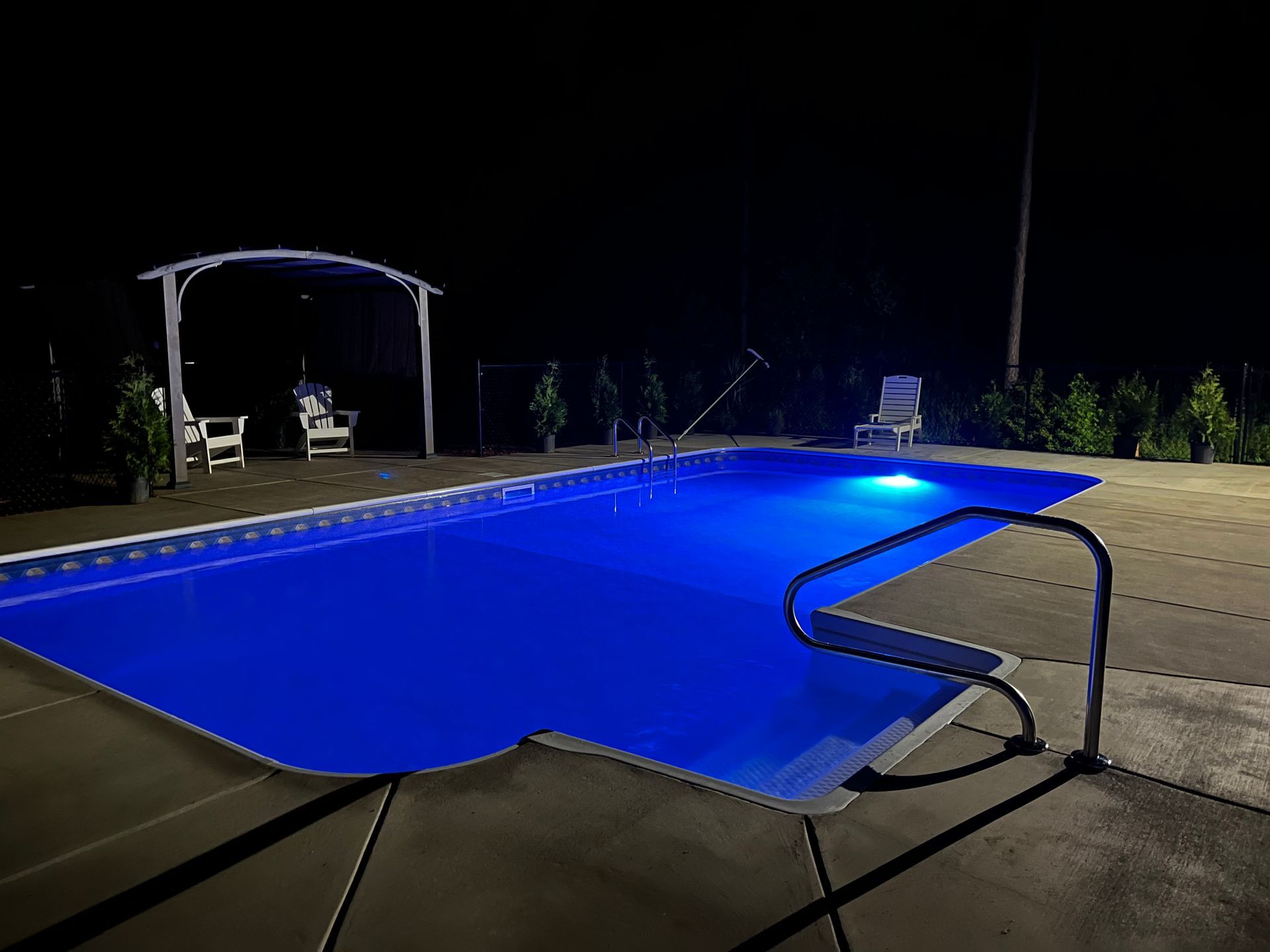 Nighttime backyard swimming pool glowing blue with a covered patio and lounge chairs nearby