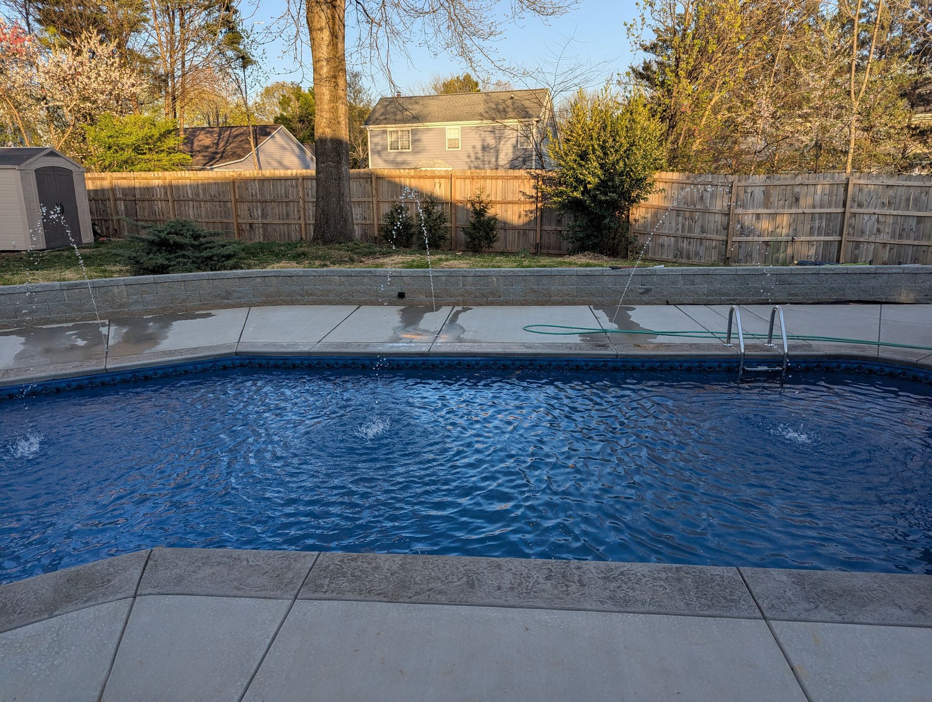 Backyard swimming pool with blue water, stone deck, and a fenced yard in the background