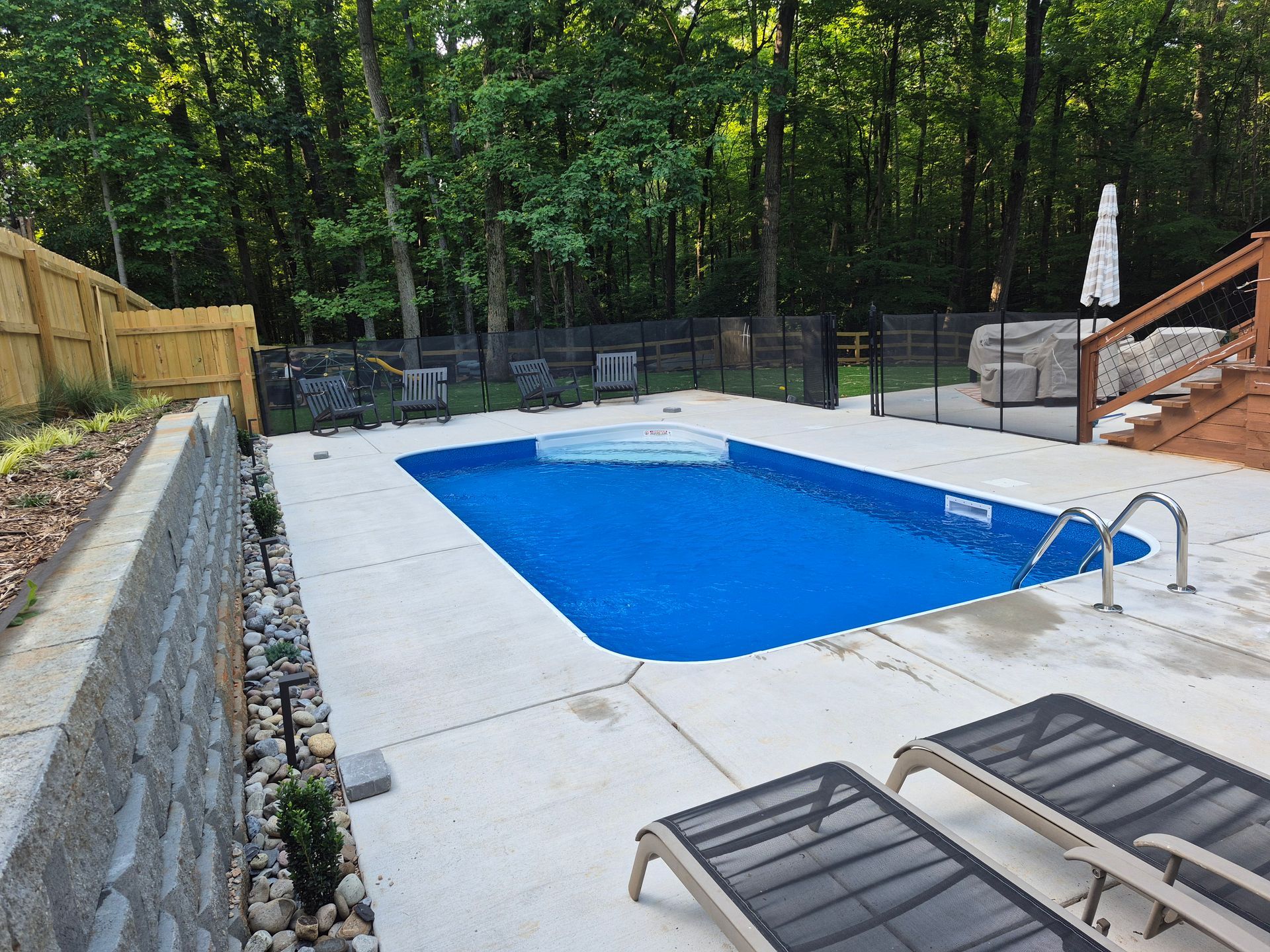 Backyard pool with blue liner, concrete deck, lounge chairs, and wooded fence line