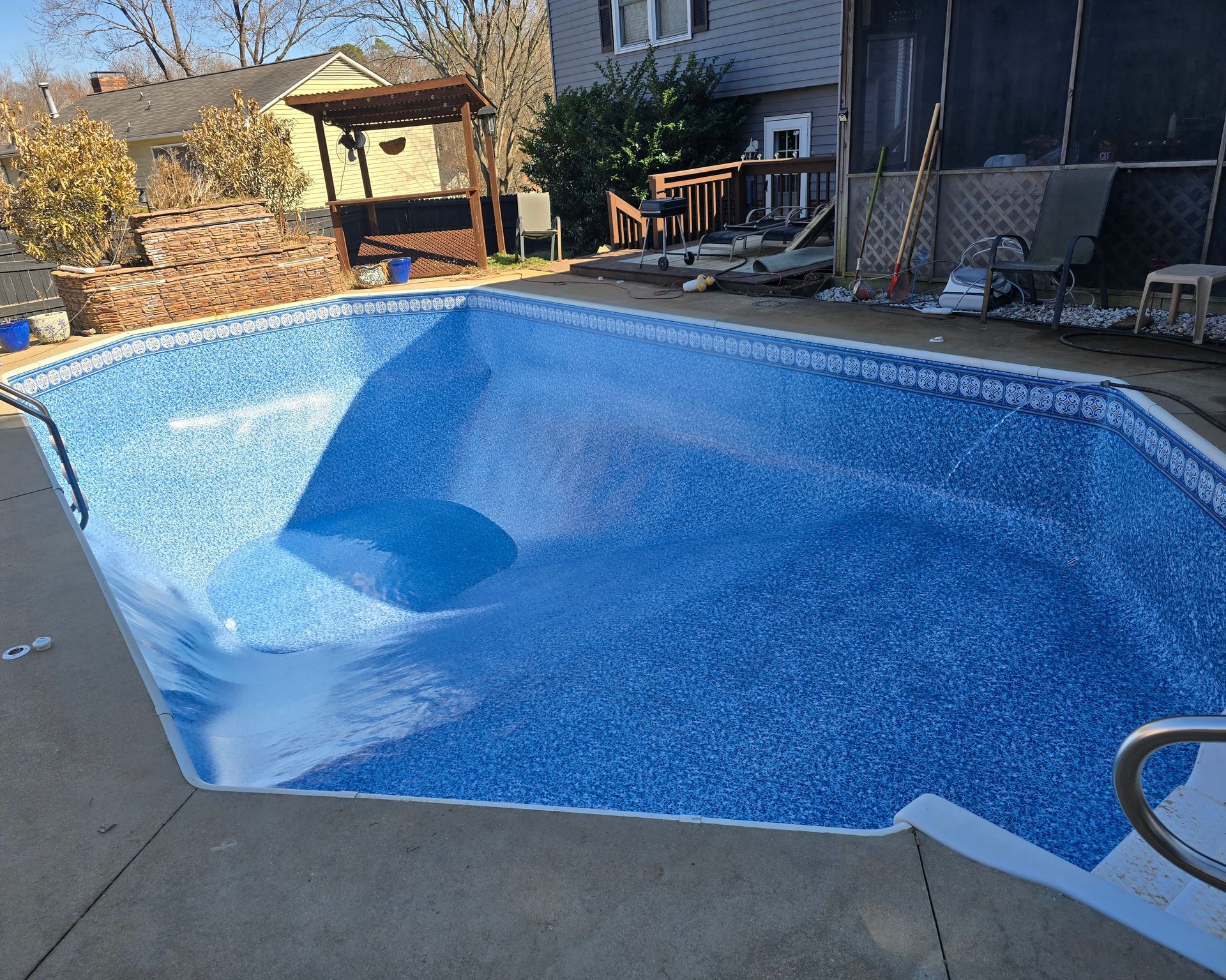 Empty blue swimming pool beside a patio and deck in a backyard