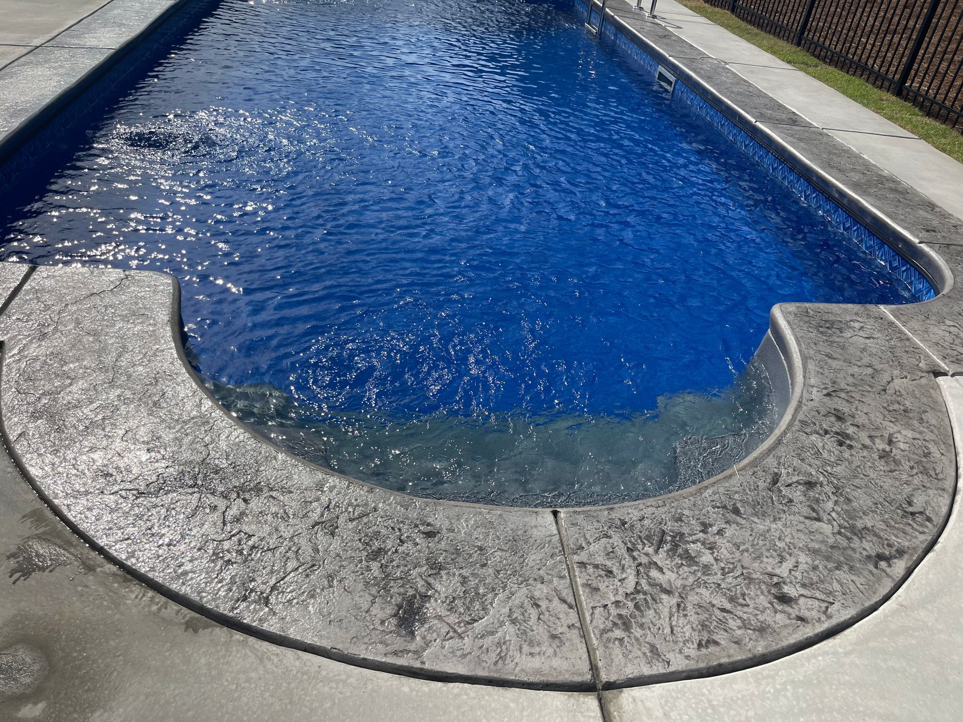 Blue swimming pool with a curved concrete edge and surrounding walkway
