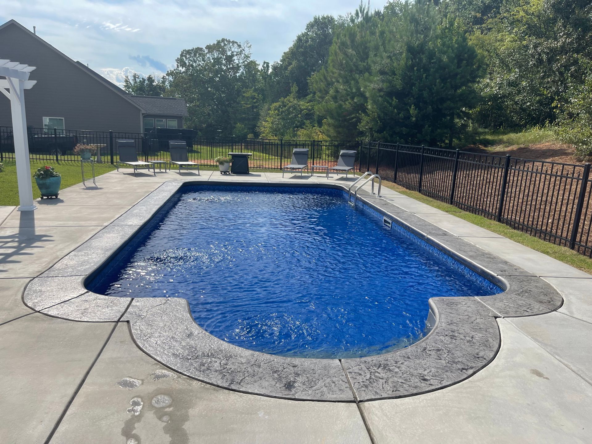 Rectangular backyard swimming pool with blue water and concrete deck under clear sky