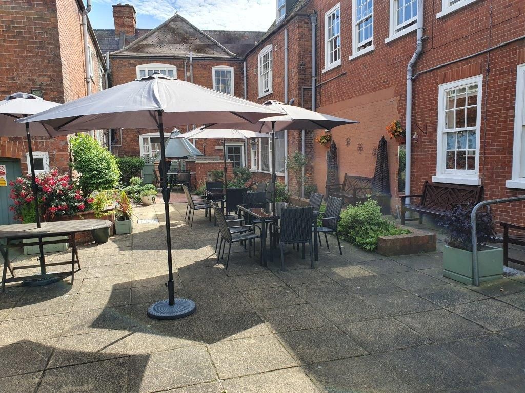 A patio with tables and chairs and umbrellas in front of a brick building.