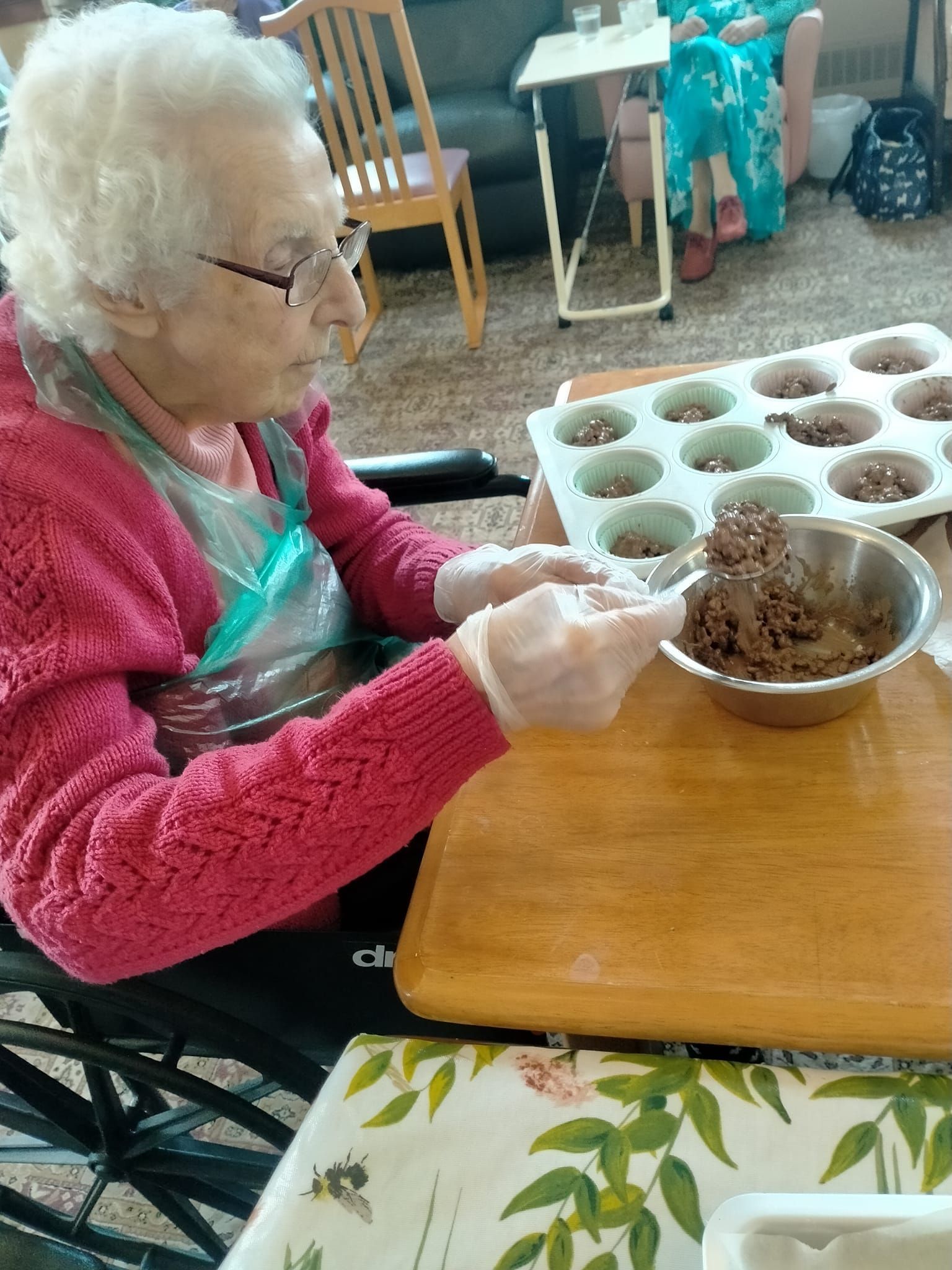 An elderly woman in a wheelchair is preparing food at a table.