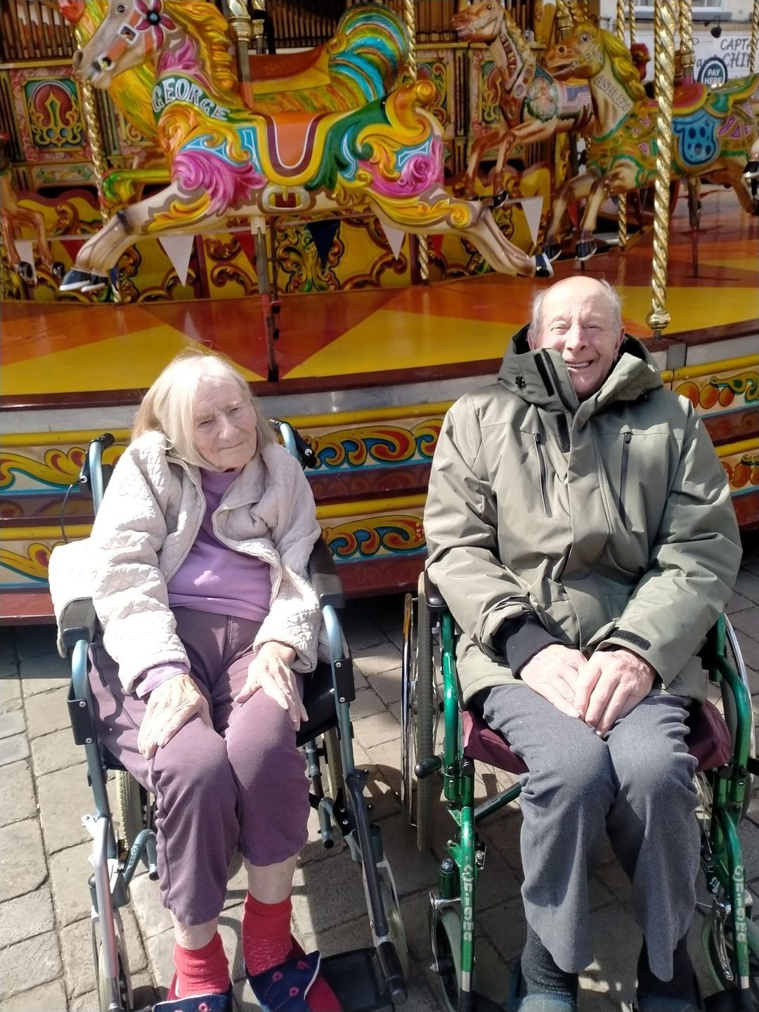 Two people in wheelchairs are sitting in front of a merry go round.