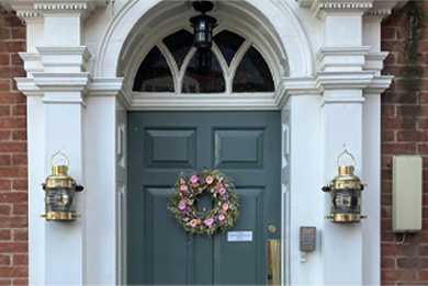 A green door with a wreath on it is on a brick building.