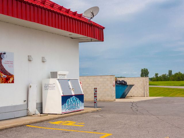 White building with red roof, vending machine, and a roadside sign in a quiet parking lot.