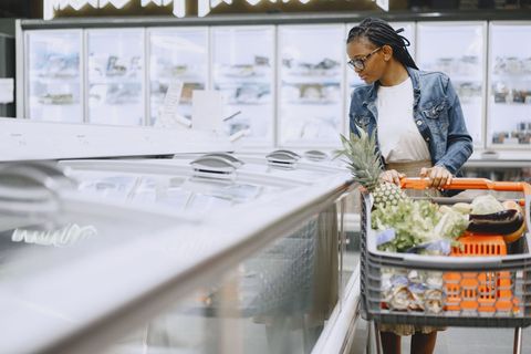 Person pushing a grocery cart in a bright supermarket aisle