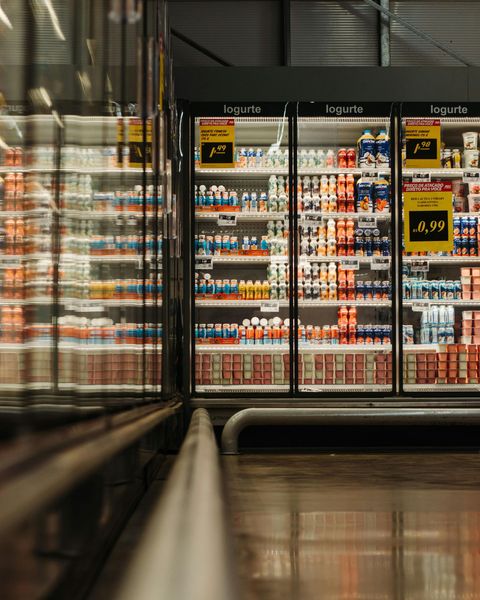 Grocery store freezer aisle with rows of drinks and frozen foods behind glass doors.