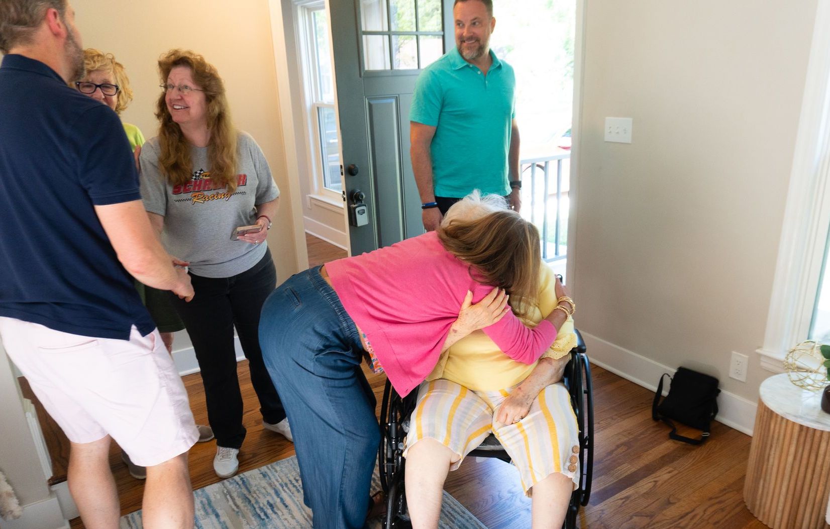 A photo of a woman hugging another senior in a wheelchair at a open house