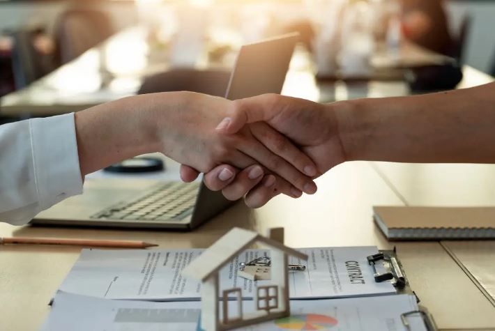 a home seller shanknig hands with a home buyer at a table