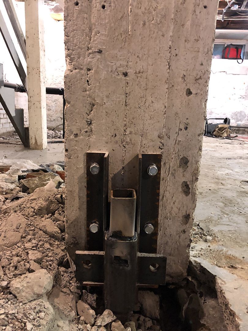 Un support métallique boulonné à la base d'une colonne en béton dans un bâtiment en construction ou en réparation.