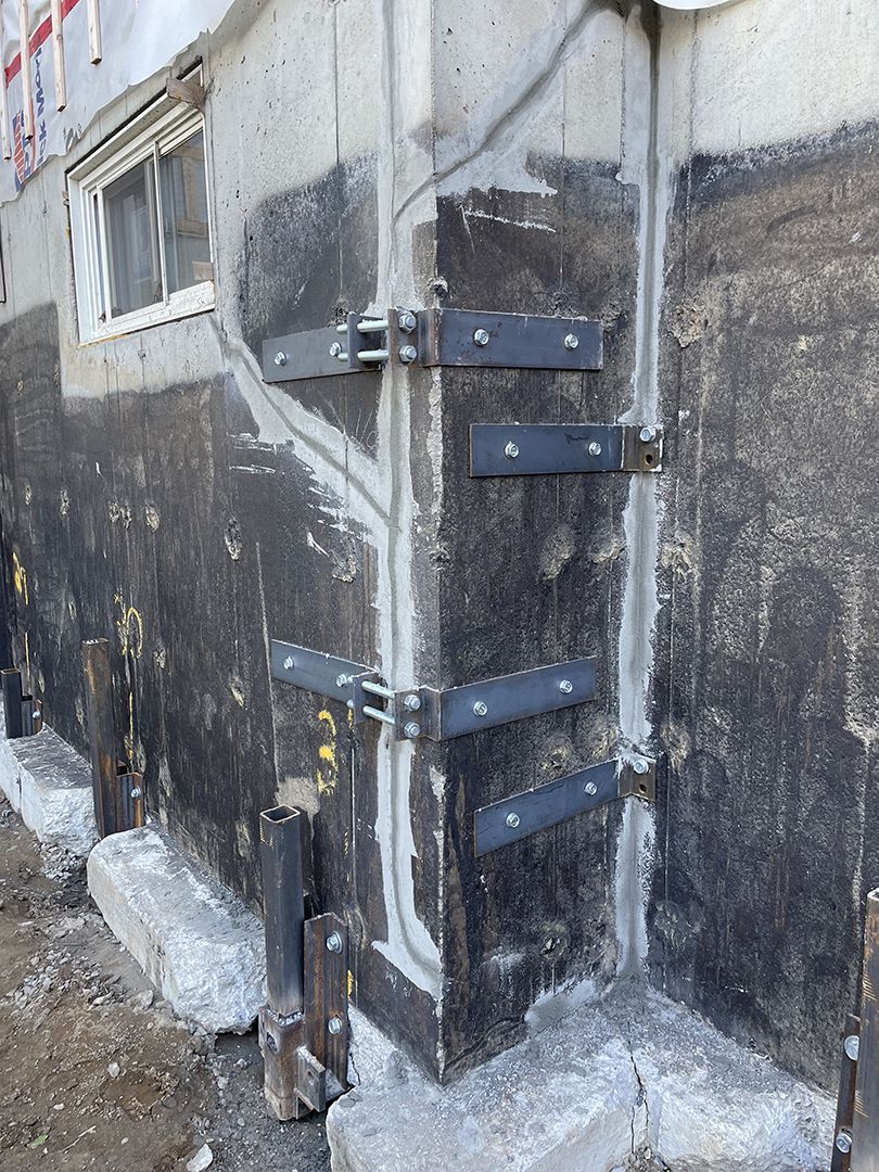 Un angle de fondation renforcé par des supports et des boulons métalliques, installé sur un revêtement étanche foncé appliqué sur des murs en béton.