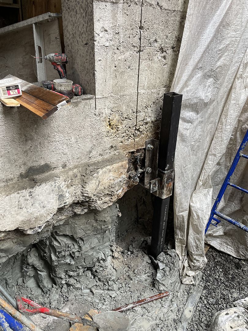 Un poteau de soutien vertical noir installé dans un trou percé dans un mur de fondation en béton lors d'un projet de construction.