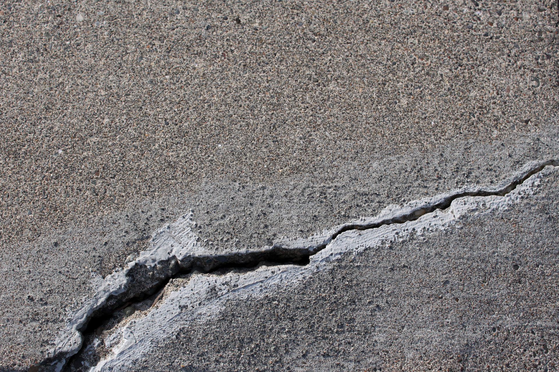 Une fissure irrégulière et proéminente fend en diagonale une surface de béton gris et rugueux.