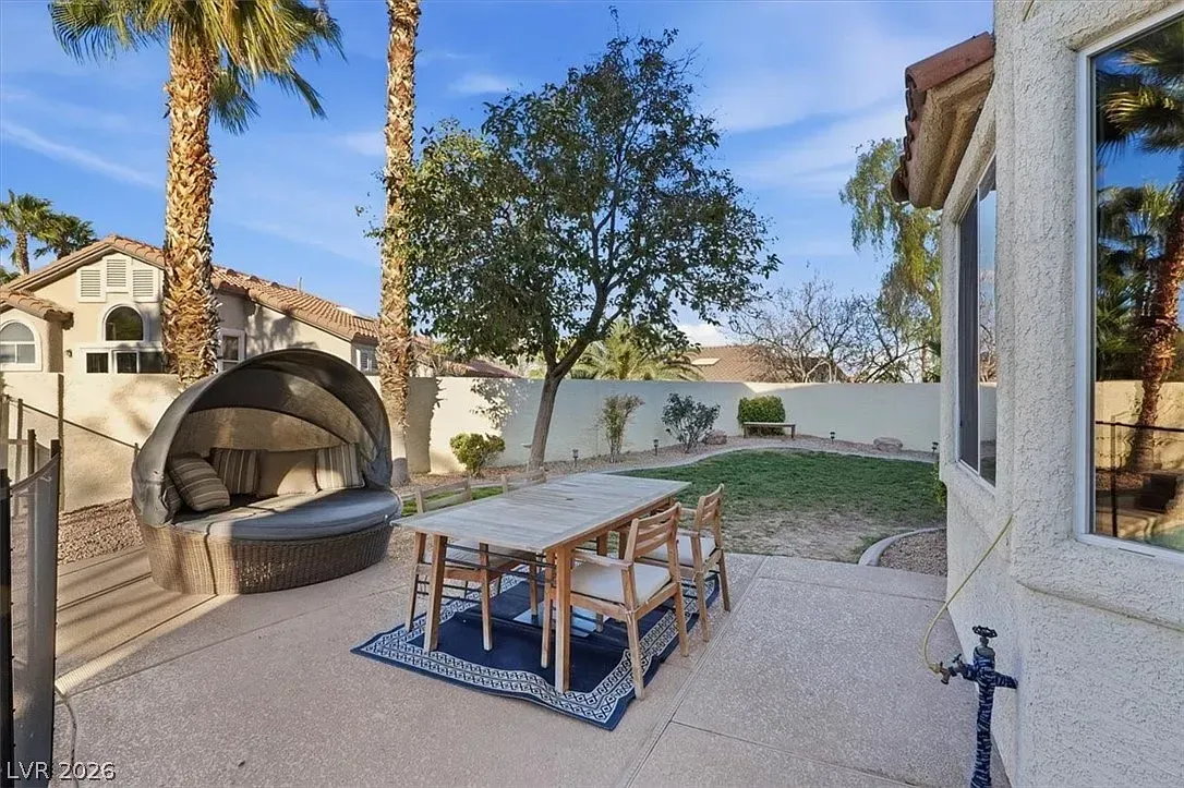 Backyard patio with picnic table, built-in grill, gravel ground, and a stucco house in the background