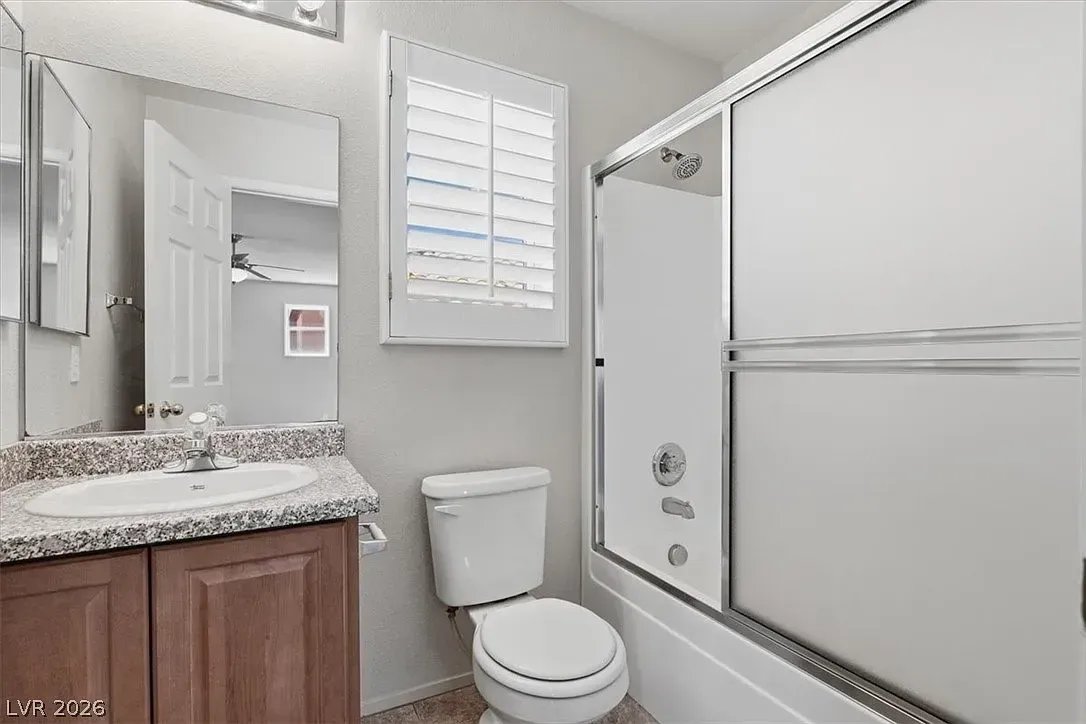 Small bathroom with toilet, sink, mirror, window, and shower/tub with sliding glass door.