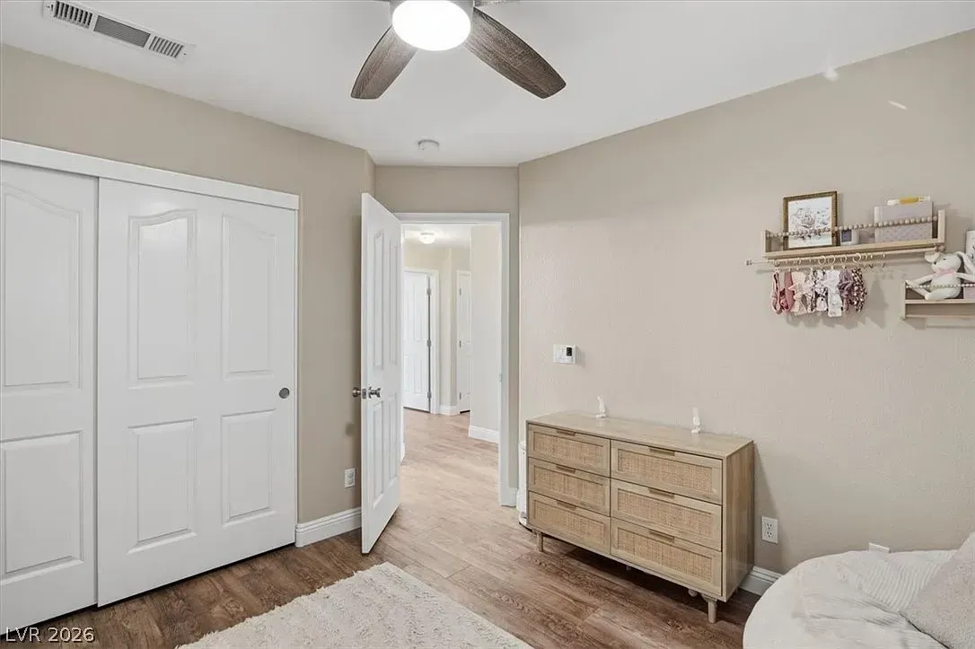 Bright bedroom with white closet doors, wicker dresser, ceiling fan, and open doorway to hall.