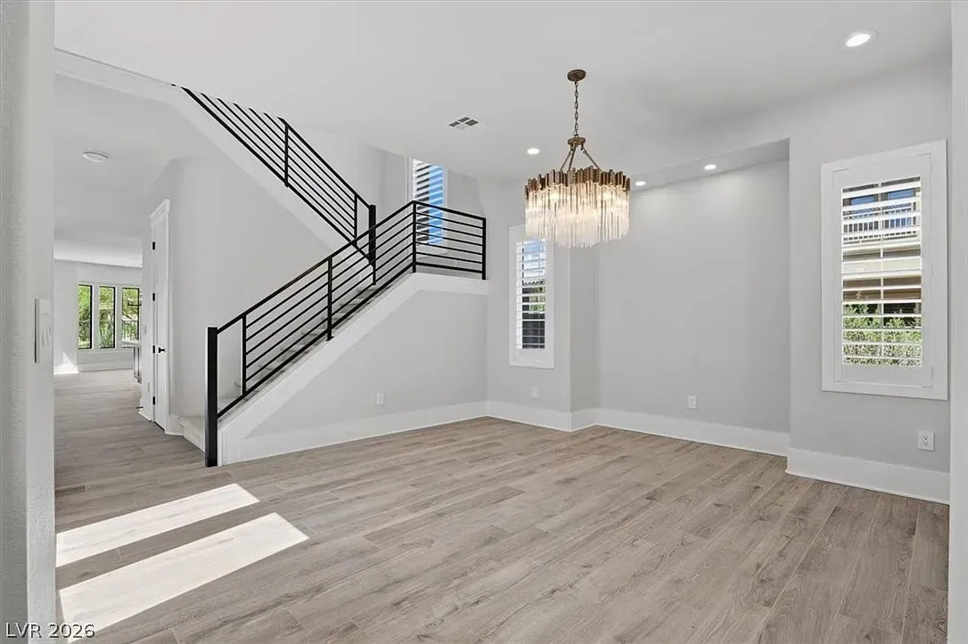 Bright empty living room with staircase, chandelier, white walls, and light wood flooring