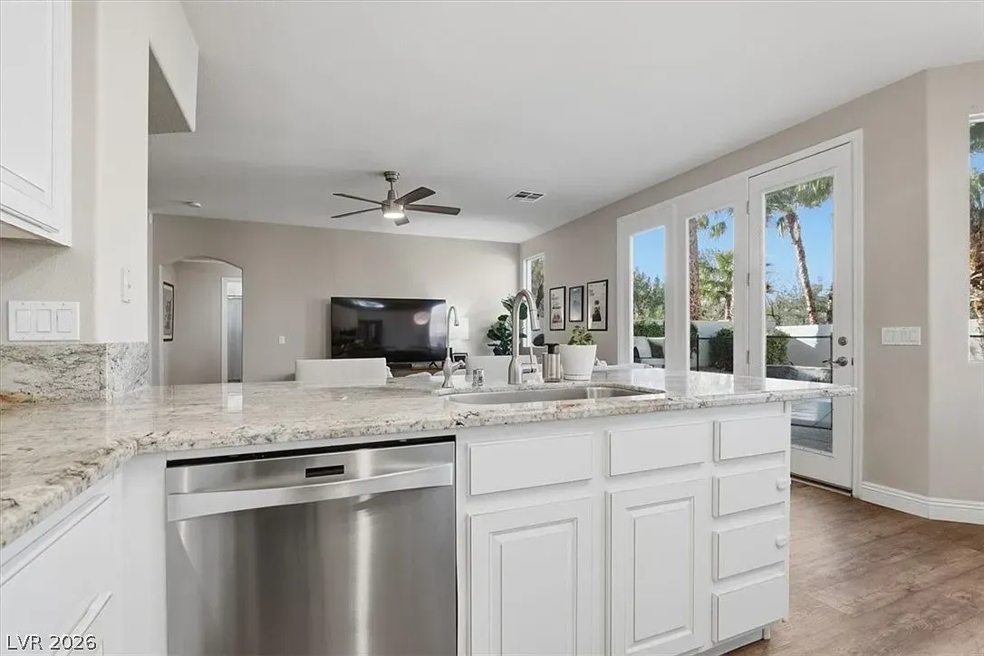 Bright modern kitchen with white cabinets, granite island, stainless dishwasher, and large windows opening to a patio