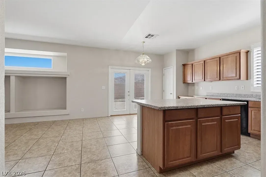 Empty kitchen with brown cabinets, granite island, tiled floor, and a small adjoining dining area.