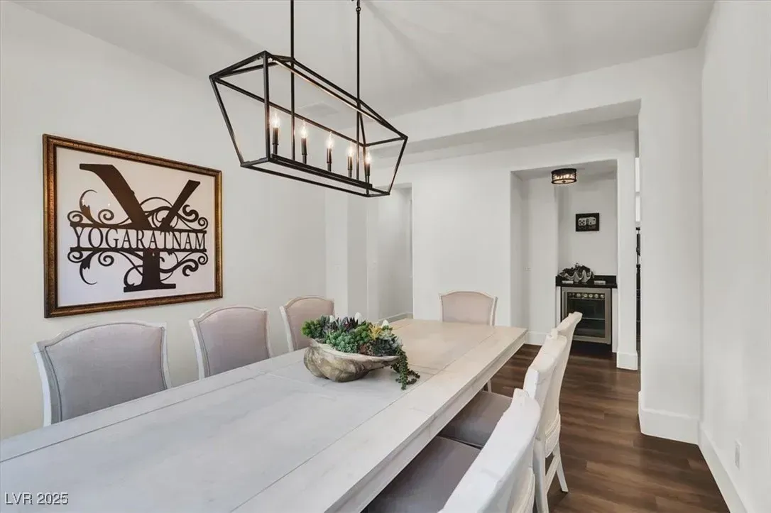 Bright dining room with a long white table, black pendant light, wall art, and dark wood floor.