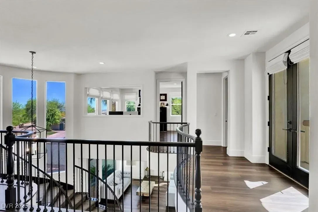 Bright upstairs hallway with black railing, hardwood floors, and sunlight from large windows and balcony doors