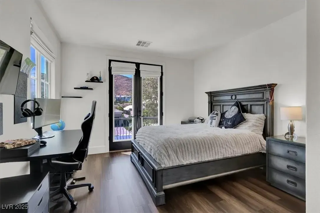 Modern bedroom with dark wood bed, gray bedding, desk chair, and open balcony doors