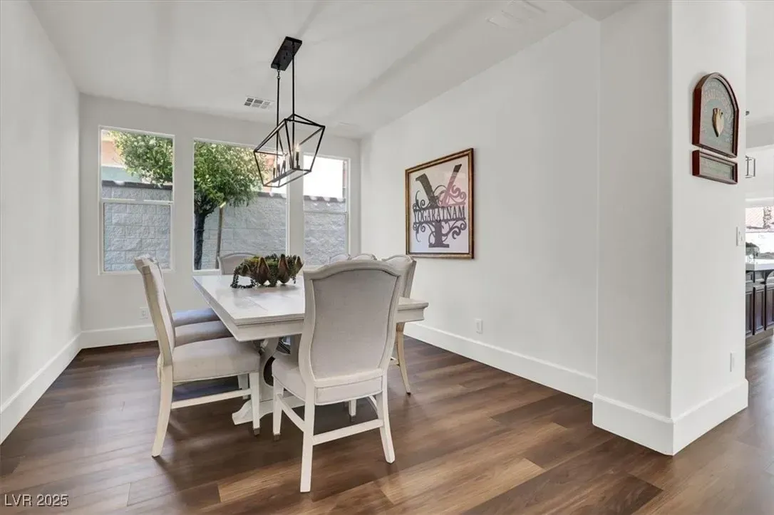 Bright dining room with white chairs, dark wood floor, and hanging pendant light