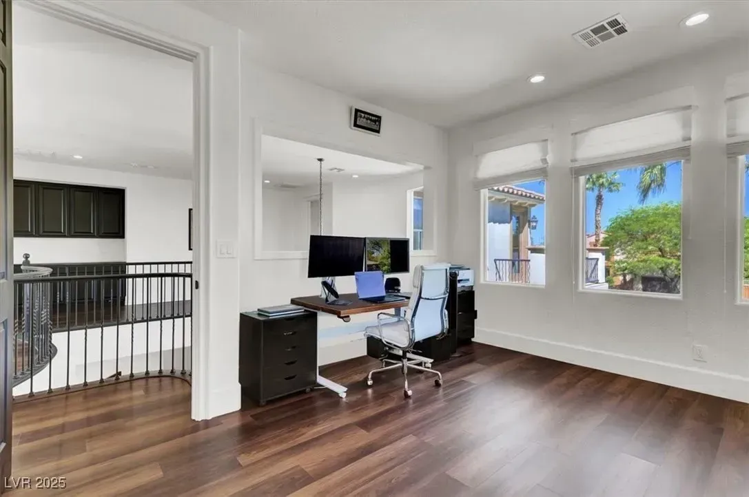 Bright home office with desk, computer, black chair, and large windows over wood floors