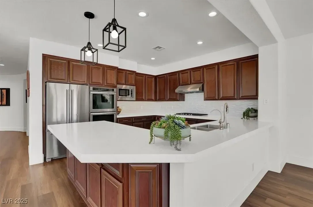 Modern kitchen with wood cabinets, stainless steel appliances, white island, and pendant lights