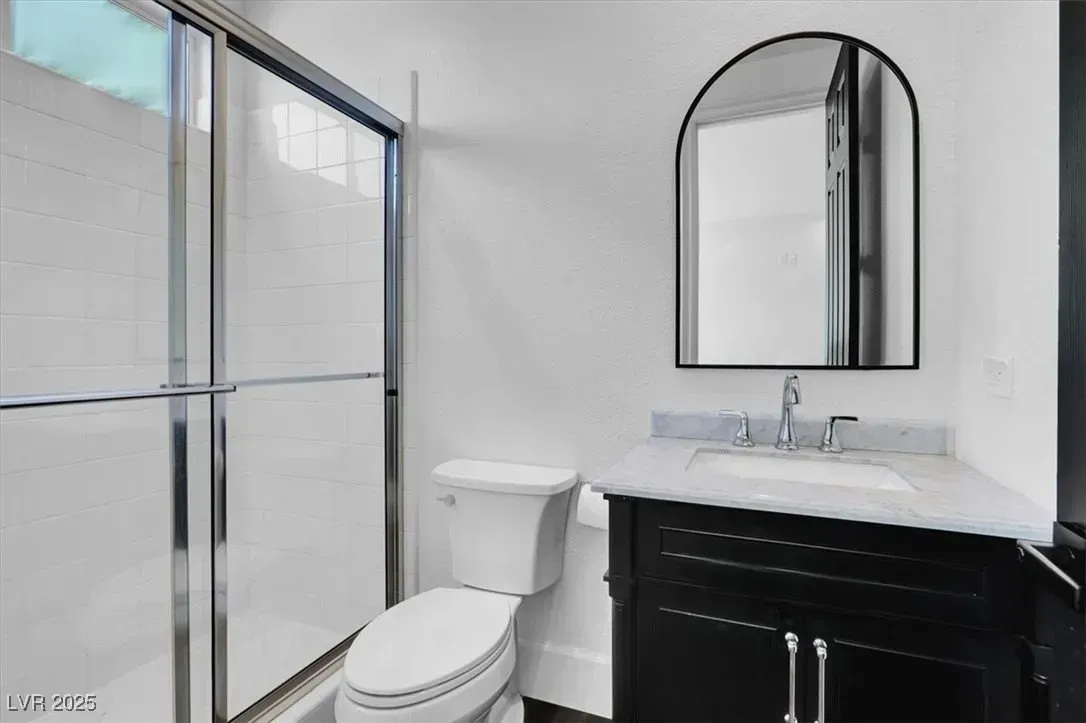 Bathroom with glass shower, toilet, and black vanity with mirror.