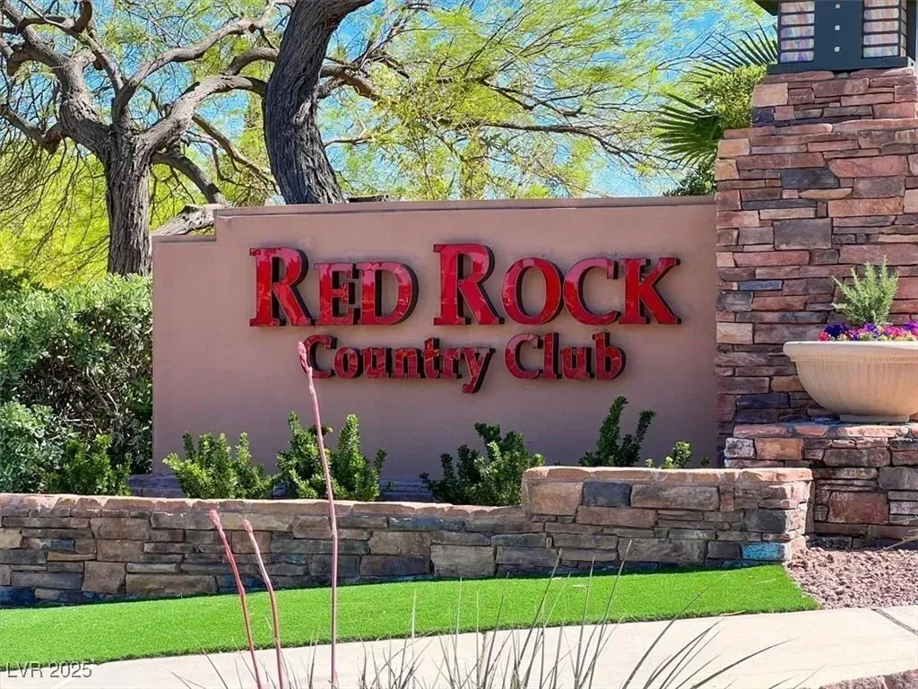 Red Rock Country Club sign by stone wall, with green lawn and trees in front.