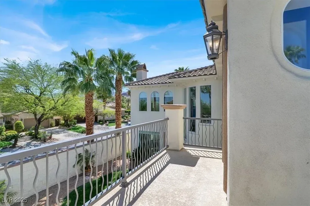 Sunlit balcony with white railing, beige stucco walls, palm trees, and blue sky view