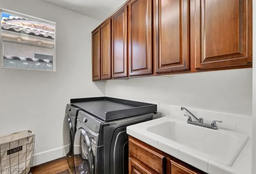 Laundry room with stacked washer and dryer, wood cabinets, utility sink, and wall-mounted storage rack.