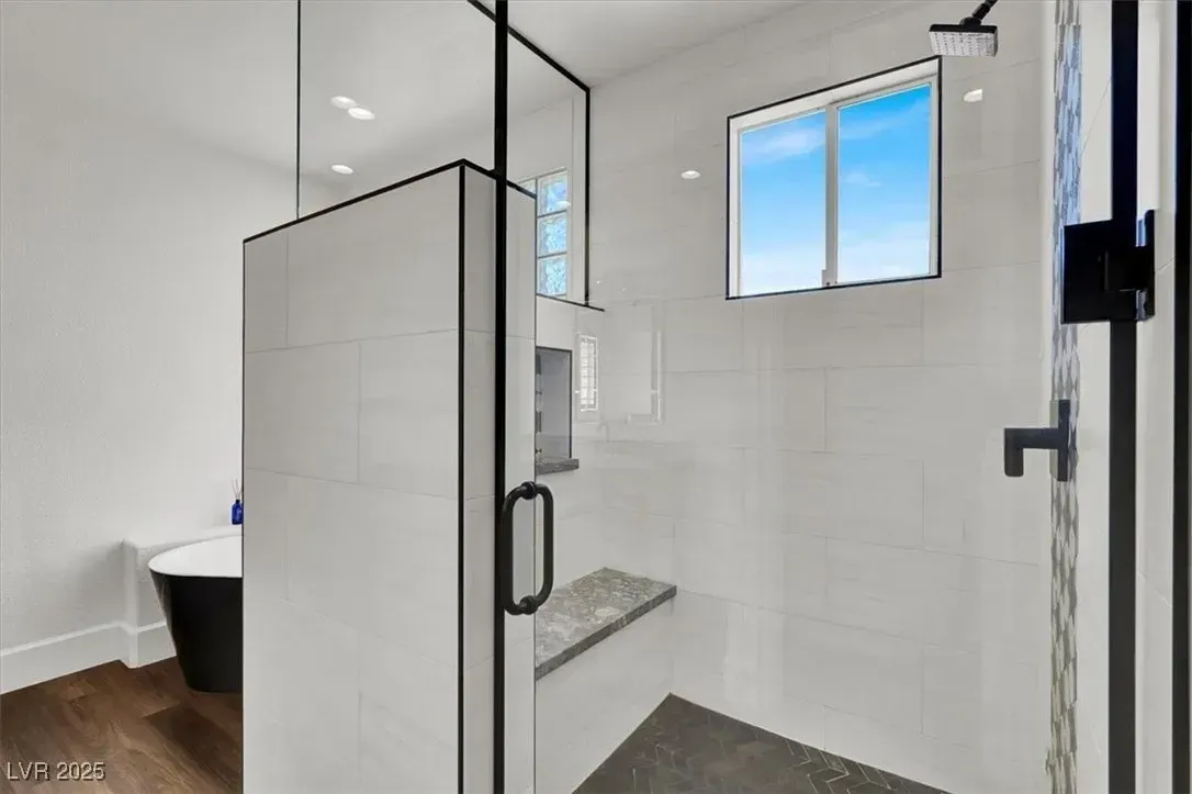 Modern tiled shower with glass door, black fixtures, window, and built-in bench