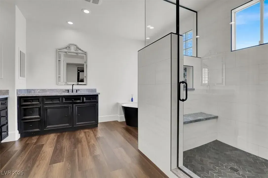 Modern bathroom with double vanity, mirror, and glass-enclosed shower with gray tile and wood floor